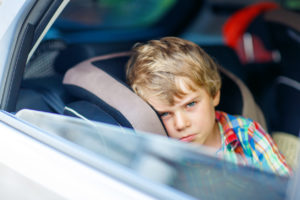 Sad little kid boy sitting in car in traffic jam during going for summer vacation with his parents. Tired, exhausted child not happy about journey.